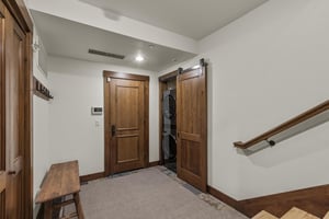 The spacious entry way has a bench to remove shoes and a stacked washer and dryer behind a barn door.