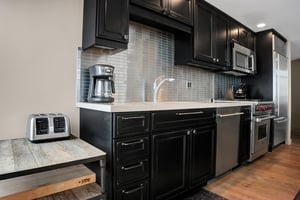 Modern kitchen with dark wood cabinetry, stone countertops, tile backsplash, coffee maker and stainless steel dishwasher.