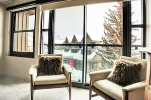 Cozy bedroom sitting area with two chairs positioned beside large windows overlooking the snowy mountain scenery.