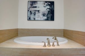 Large soaking tub with neutral tile surround, brushed metal fixtures and contemporary artwork above.
