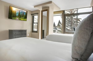 Bright guest bedroom with two twins beds, wallmounted TV and large windows overlooking the snowy mountain scenery.