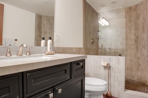 Full bathroom with dark wood vanity, stone countertop, large mirror and glassenclosed walkin shower.