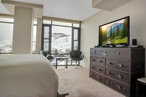 King bedroom with dresser, TV, sitting area and large windows overlooking the snowy mountains.