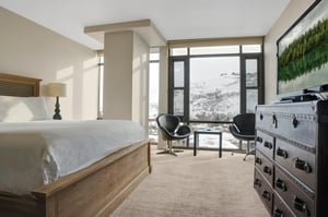 Spacious king bedroom with sitting area and floortoceiling windows overlooking the snowy mountains.