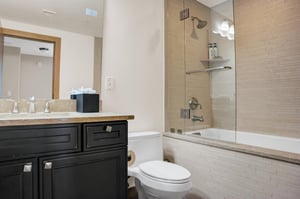 Bathroom with tub and shower combination, toilet, vanity and modern dark cabinetry.