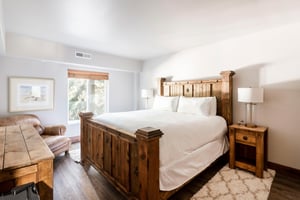Bright bedroom with rustic wood king bed, white linens, nightstands and natural light.