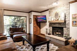 Cozy living room with stone fireplace, wallmounted TV, leather seating and large windows.