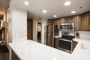 Renovated kitchen with white countertops, wood cabinetry and stainless steel appliances.