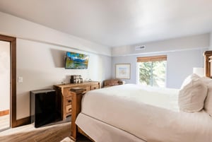 Bright bedroom with rustic wood bed, wallmounted TV, dresser and window overlooking the trees.