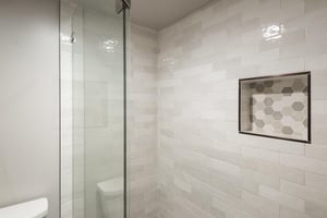 Glassenclosed walkin shower with white tile surround and builtin shower niche.