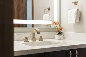 Bathroom vanity with white stone countertop, modern fixtures and illuminated mirror.