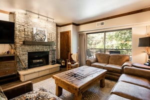Living room with stone fireplace, leather seating, rustic wood coffee table and sliding doors to the balcony.