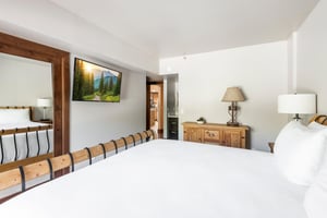 Primary bedroom with woodframed bed, wallmounted TV, dresser and warm wood accents.
