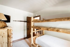 Rustic log bunk beds with white linens in a cozy guest bedroom.
