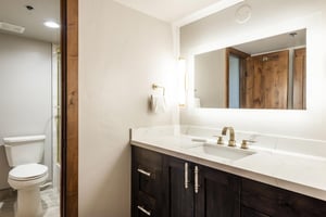 Full bathroom with dark wood vanity, white countertop, large illuminated mirror and modern fixtures.