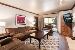 Unit 227 living room with leather sectional, wood coffee table, area rug and large patio doors.