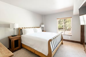 Unit 229 bedroom with woodframed bed, white linens, nightstands and large window overlooking the trees.