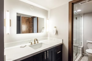 Unit 229 ensuite bathroom with dark wood vanity, white countertop, large mirror and glassenclosed shower.