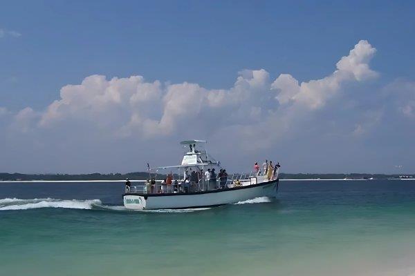 Passengers aboard a dolphin tour boat cruising through clear emerald waters near Pensacola Beach.