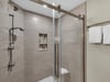 Step into your spacious glassenclosed shower with elegant woodgrain tiles and modern fixtures for your daily refresh.