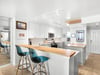 The modern kitchen features sleek white cabinets, warm wood countertops, and stylish turquoise bar seating