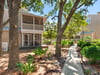 Shaded pathways and mature trees surround the property building, with multilevel balconies overlooking manicured gardens and peaceful greenery throughout the neighborhood.
