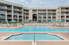 Beachfront resort featuring a sparkling pool, hot tub, and multiple balconies under sunny skies—your coastal retreat awaits.