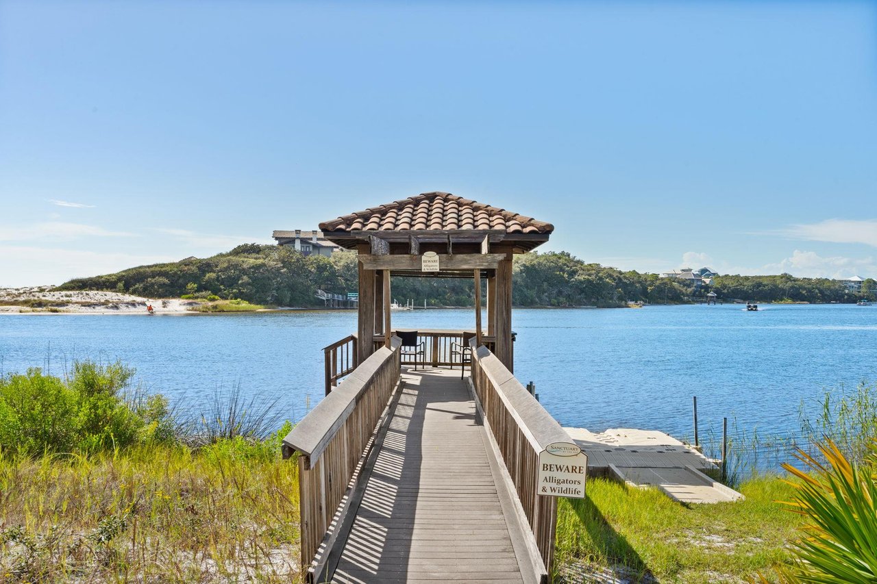 2191164 A Wooden Dock Leading To A Small Building On A Body Of Water