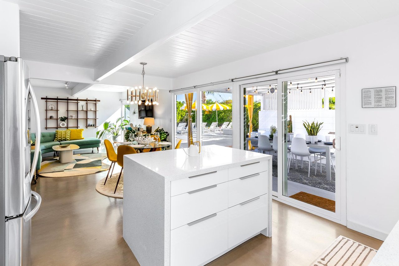 Open concept kitchen, living and dining with walls of glass looking out at the pool
