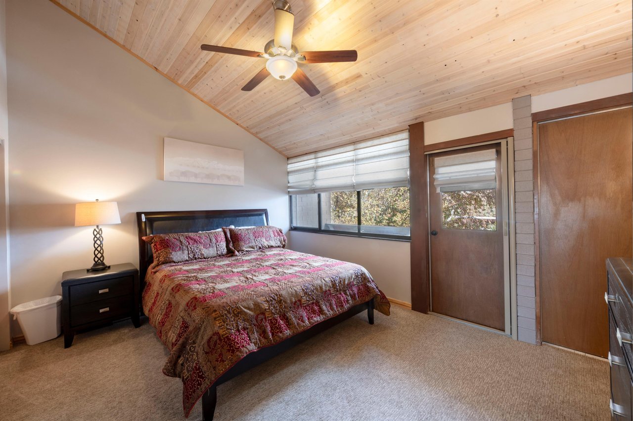 Rest easy in the spacious king master bedroom at Park Avenue 235, featuring vaulted wood ceilings, a ceiling fan, and peaceful natural light.