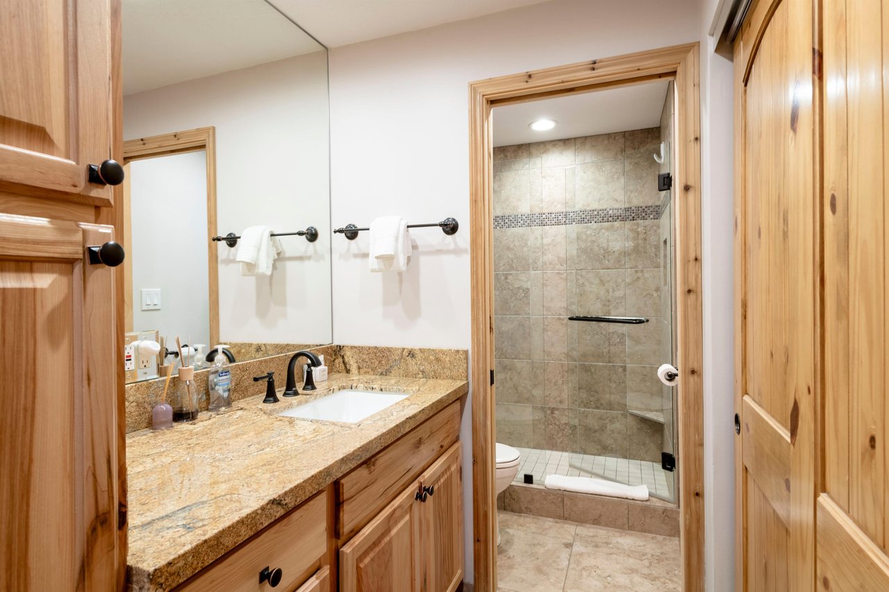 A beautifully updated full bathroom at Park Avenue 235 features a granite vanity, walkin tile shower, and warm, modern finishes.