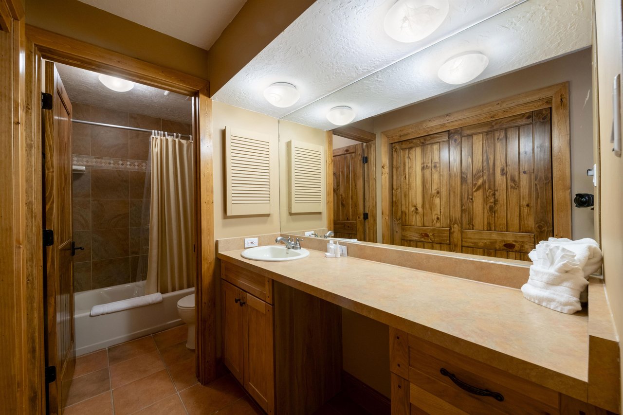 The full bathroom at Park Avenue 224 features warm wood cabinetry, a wide vanity, and a tubshower combo — everything you need to unwind during your Park City lodging stay.