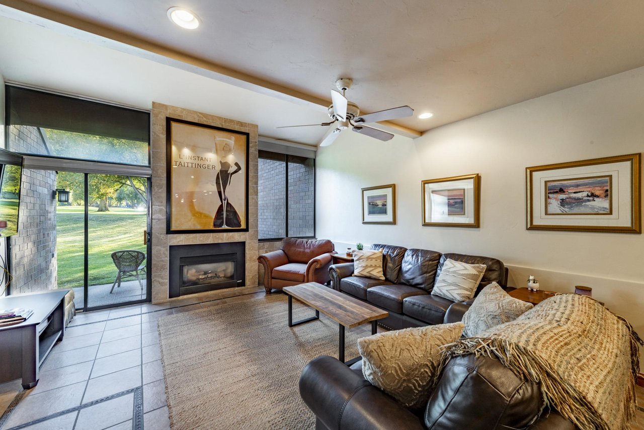The stylish living room at Park Avenue 245 features rich leather furnishings, a sleek fireplace, and a wall of windows overlooking the outdoors — a refined retreat for your Park City condo rental stay