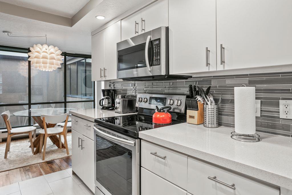 The fully equipped modern kitchen at Park Avenue 296 features stainless steel appliances, crisp white cabinetry, and elegant tile backsplash. Everything you need to cook and entertain during your Park