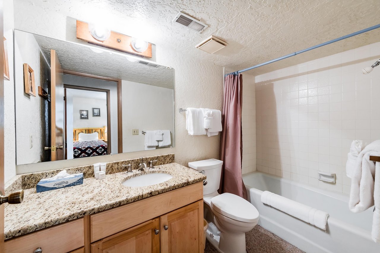 Fresh, clean, and thoughtfully stocked, this full bathroom at Temptation 8 features warm granite countertops, wood cabinetry, and a tub and shower combo — all the essentials for a comfortable Park Cit