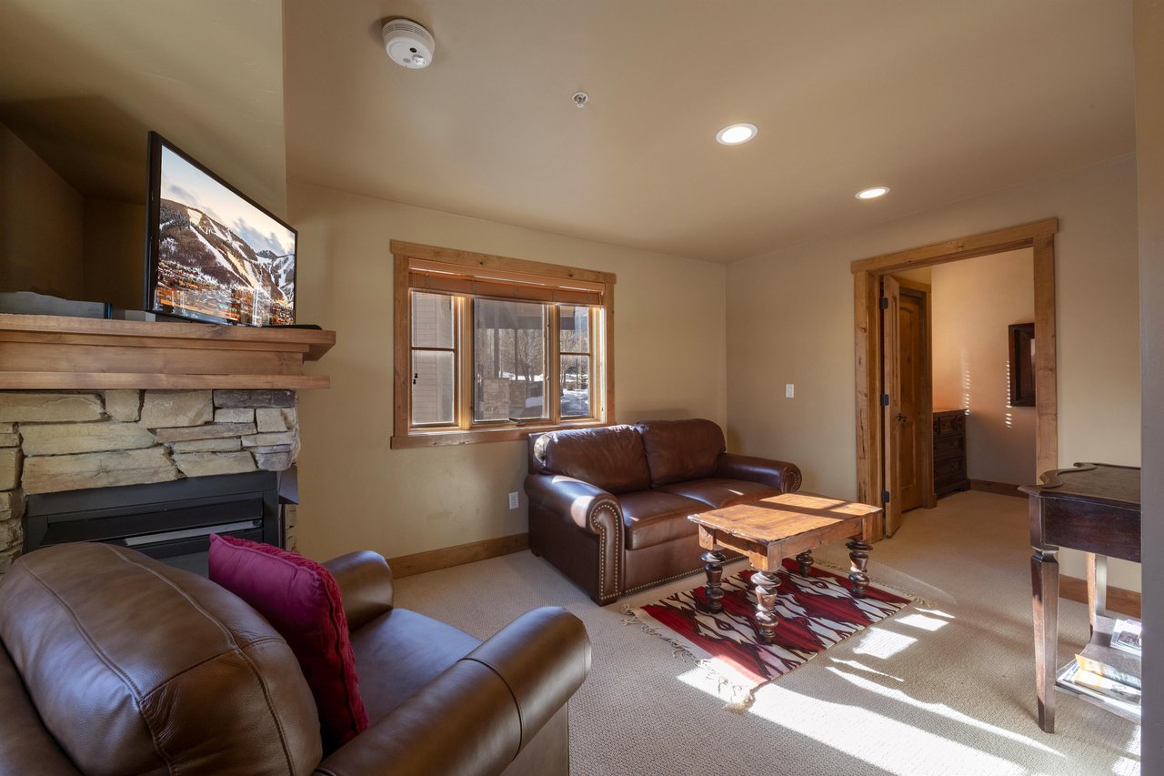 Cozy up by the stone fireplace in the living room at Jupiter Inn 10. With comfortable leather seating and plenty of natural light, this Park City condo rental is a welcoming mountain retreat.