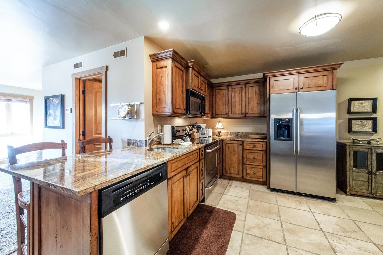 The fully equipped kitchen at Jupiter Inn 17 boasts stainless steel appliances, granite countertops, and rich wood cabinetry — everything you need to feel at home in this Park City vacation rental.