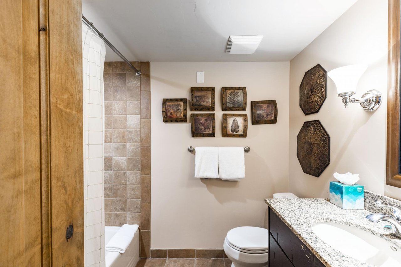 The charming bathroom at Jupiter Inn 18 features granite countertops, a tub and shower combo, and unique decorative touches that add character to this Park City vacation rental.