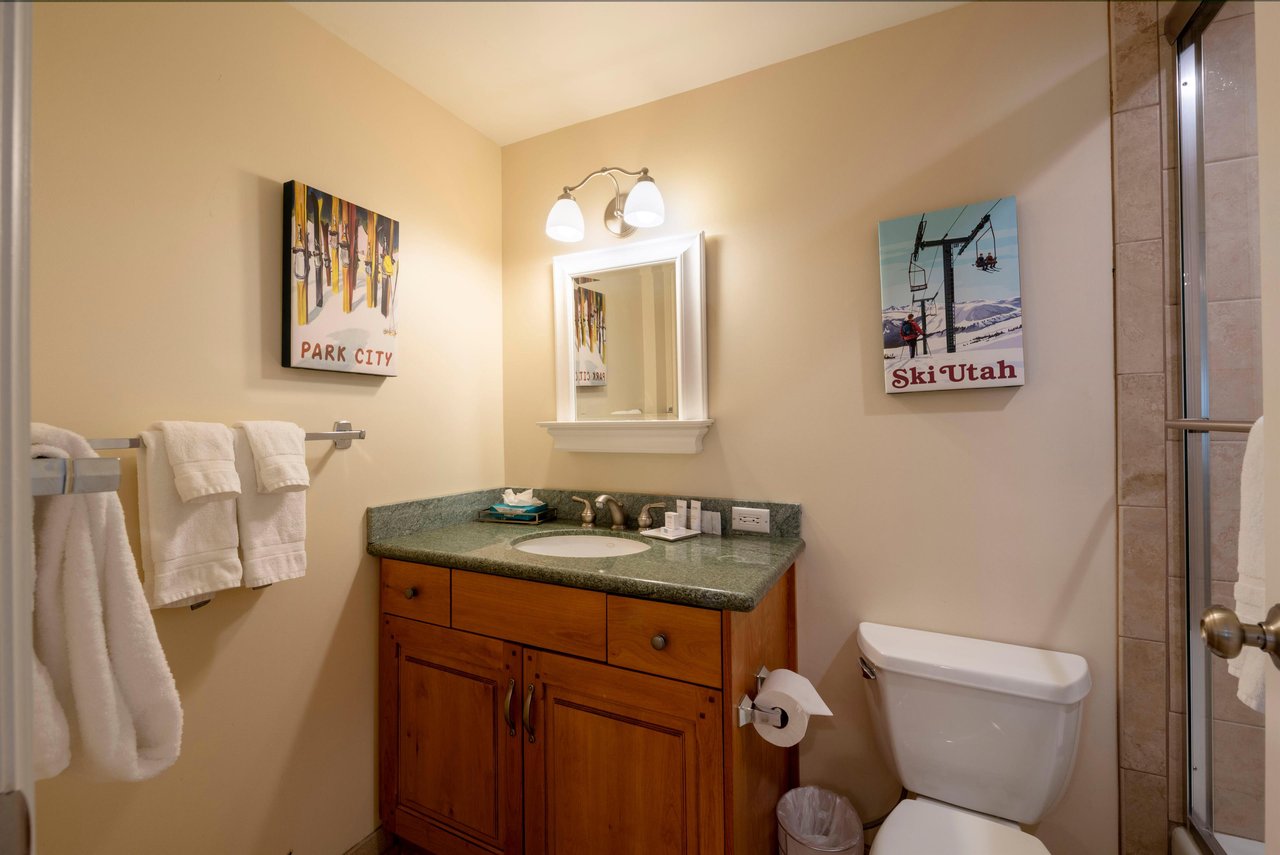 The thoughtful details continue in this guest bathroom at Resort Plaza 5004 — featuring classic wood vanity and playful local artwork, this Park City condo rental nails the perfect mountain getaway vi