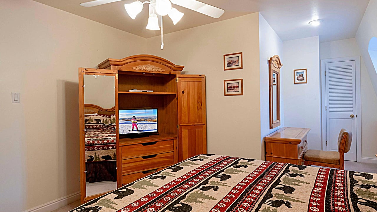 Relax in the wellfurnished king bedroom at Resort Plaza 5013 — a cozy Park City vacation rental complete with an entertainment armoire and charming mountainthemed décor.