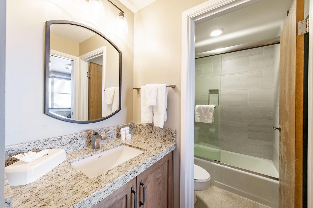 This tastefully updated bathroom features a granite vanity, warm wood cabinetry, and a sleek glassenclosed shower, offering a clean and comfortable space to refresh after a day on the mountain.