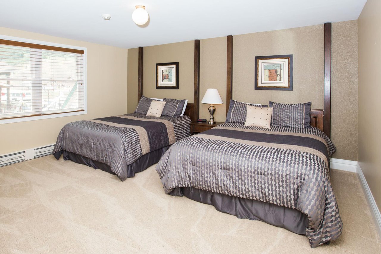 This stylishly appointed double queen bedroom features elegant bedding, warm wood accents, and a bright window, providing a sophisticated and restful space for guests at this Park City vacation rental