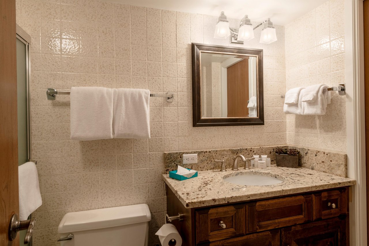 This charming bathroom features warm wood cabinetry, granite countertops, and classic tile detailing, providing a clean and comfortable space for guests during their Park City vacation rental stay.