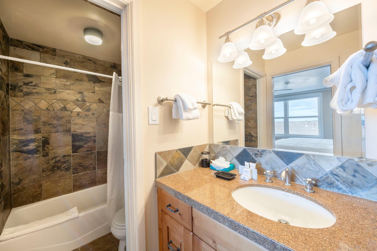 Resort Plaza 5052 continues to impress with another beautifully appointed bathroom, featuring warm stone tile accents, a generous vanity, and a combination tub and shower that add a touch of spalike