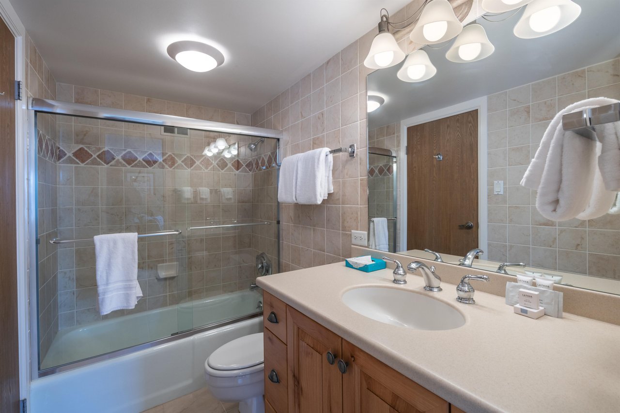 Resort Plaza 5064 continues to impress with a clean and wellappointed bathroom featuring a glassenclosed tub and shower, warm tile accents, and a spacious vanity that add a refreshing touch of comfo