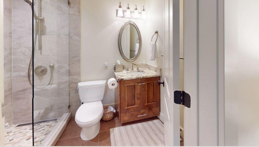 Three Kings 64 impresses with a beautifully designed bathroom featuring warm wooden cabinetry, a elegant oval mirror, and stunning marble tile accents that add a touch of spalike luxury to this excep