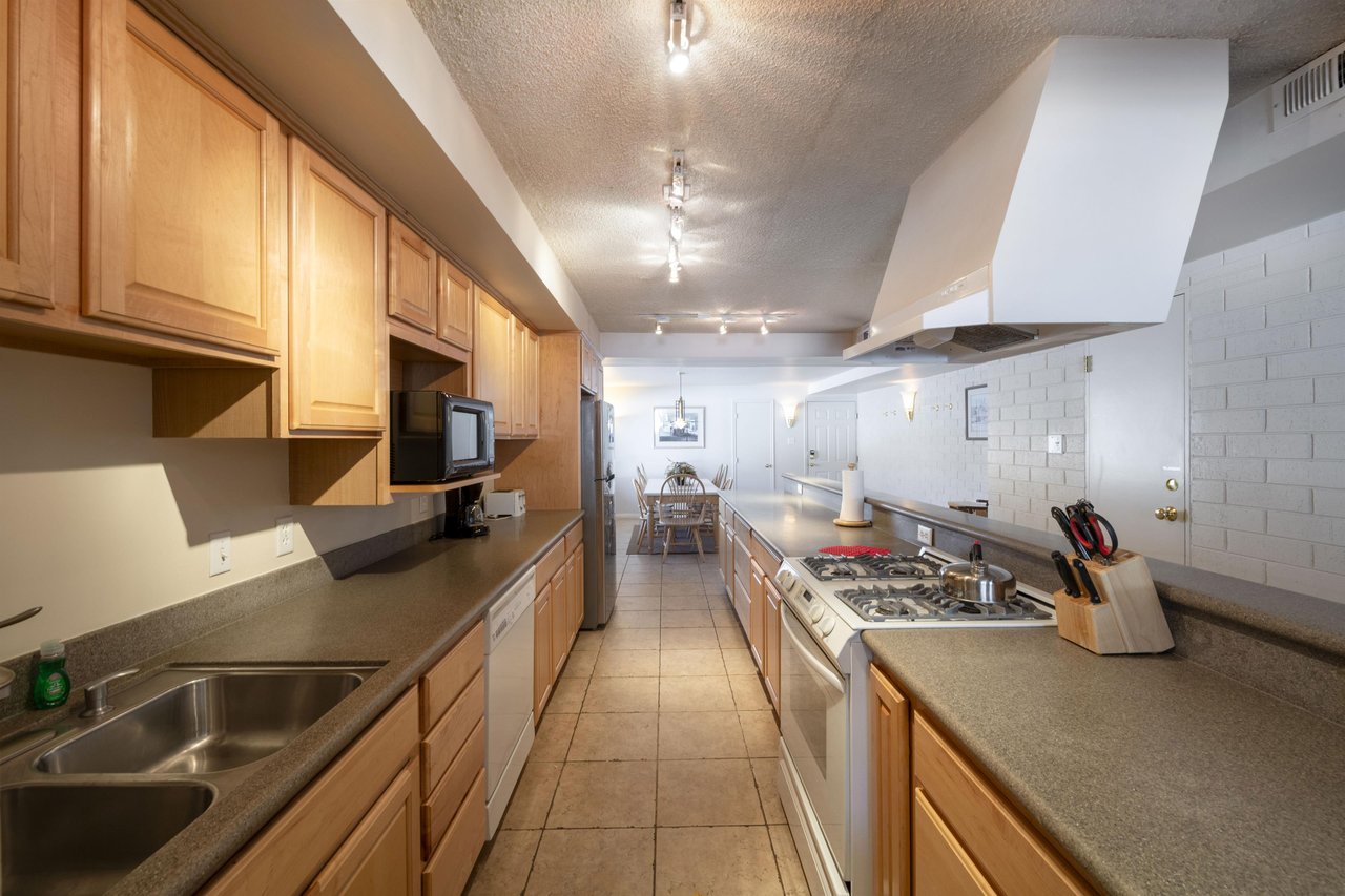 The generously sized galley kitchen at Park Avenue 251 offers abundant counter space, warm wood cabinetry, and a full suite of appliances — providing everything you need for effortless home cooking du