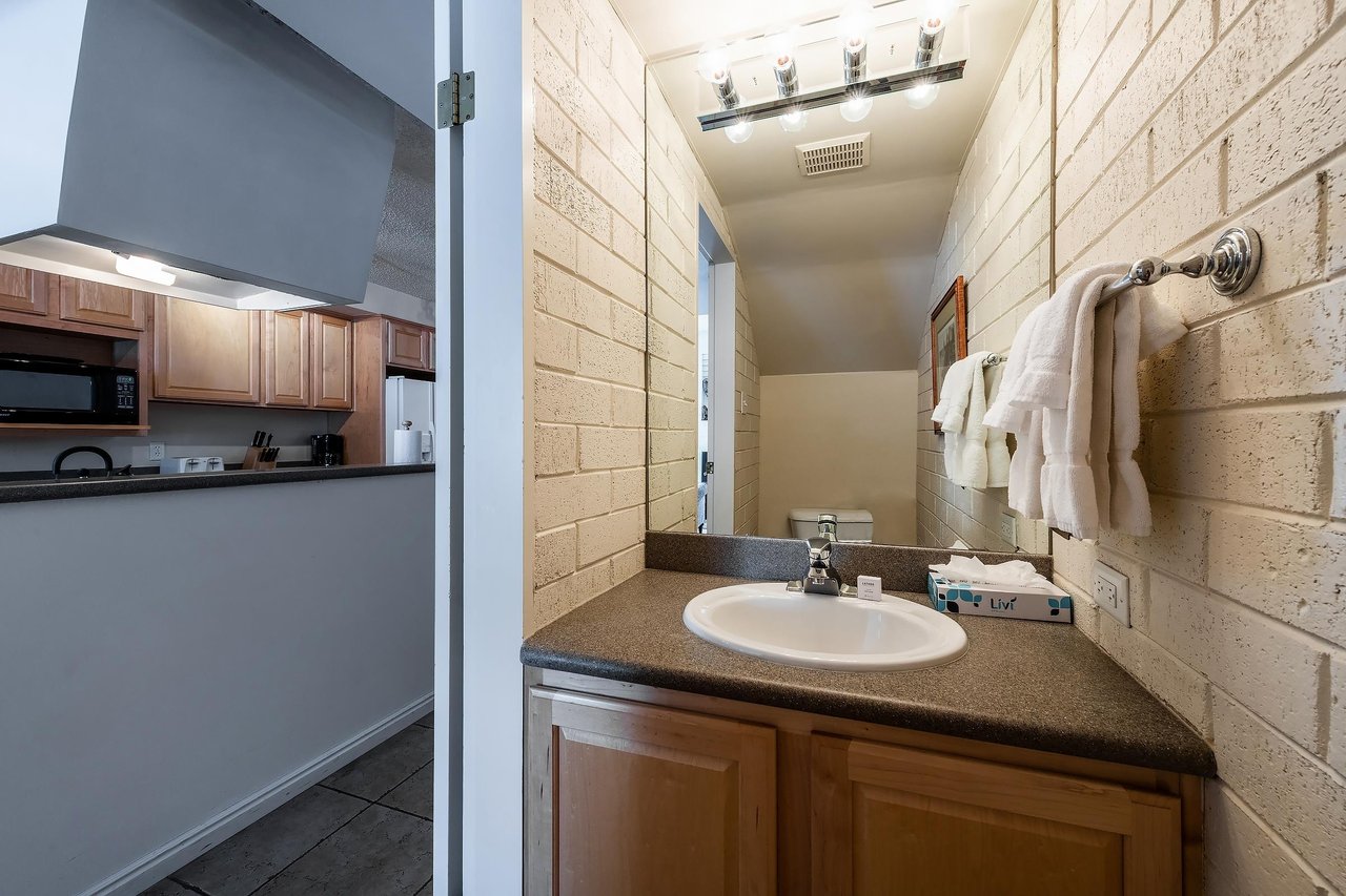 The conveniently located main level half bathroom at Park Avenue 251 features warm wood cabinetry and a classic brick accent wall, adding a charming and practical touch to this wellappointed Park Cit