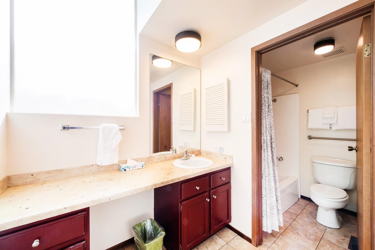 The wellappointed bathroom at Park Avenue 267 features a dual vanity with rich wood cabinetry and warm countertops, providing ample space and comfort for every guest.
