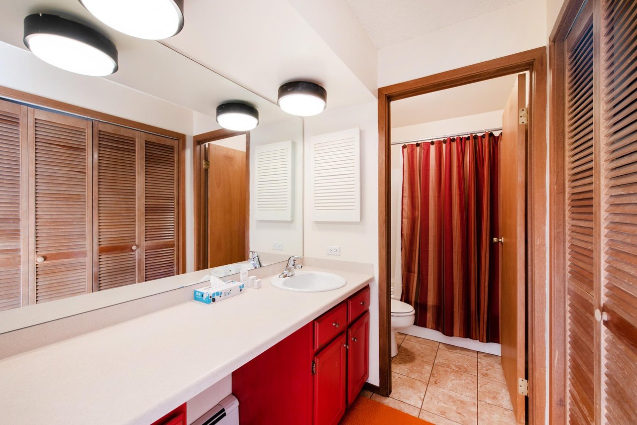 The spacious bathroom at Park Avenue 267 features a large vanity, louvered wood cabinet doors, and a separate shower and toilet area.